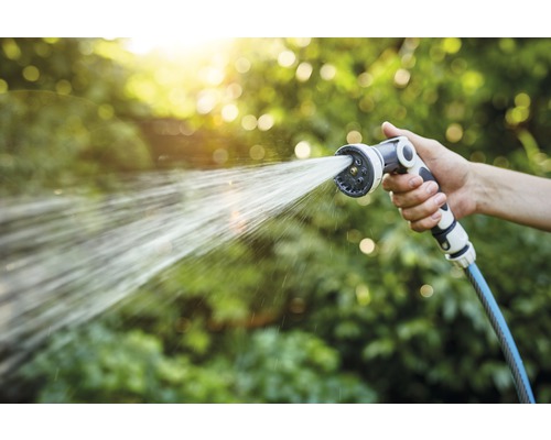 Hand houdt tuinslang met sproeikop vast die water sproeit