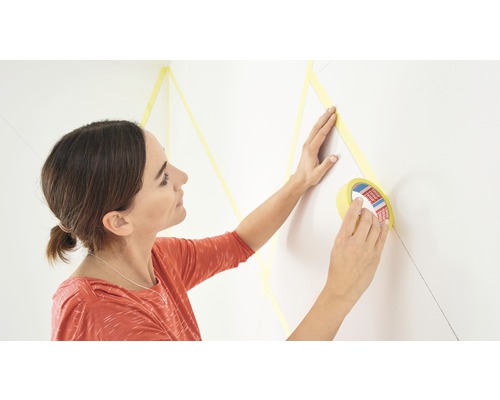 TESA Precision Indoor Schilderstape 25 m x 25 mm 2 stuks Vrouw plakt schilderstape op een muur voor decoratief schilderen