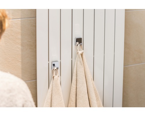 Witte radiator met twee handdoeken en chromen haken in de badkamer.