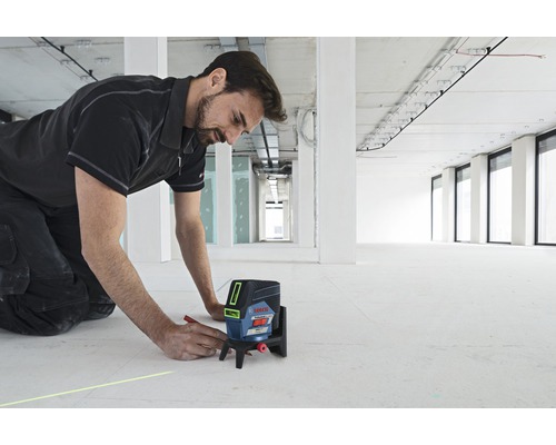 Een man gebruikt een Bosch kruislijnlaser op een bouwplaats om een lijn op de vloer te tekenen.