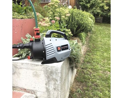 Tuinpomp met slang op een betonnen voetstuk in de tuin