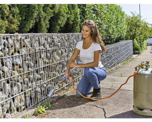 Vrouw verwijdert onkruid met een gasbrander tegen een schanskorfmuur