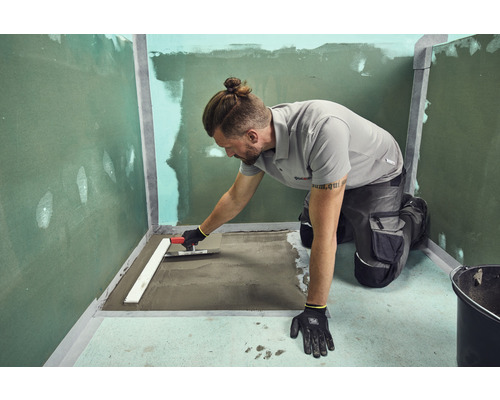 Ambachtsman die met een troffel egalisatiemortel verdeelt in een badkamer