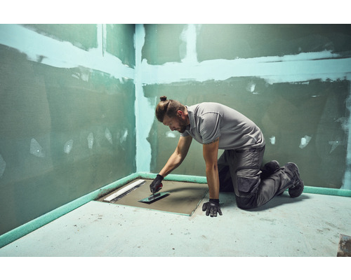 Ambachtsman bezig met het werken aan een gelijkvloerse douche met een plamuurmes