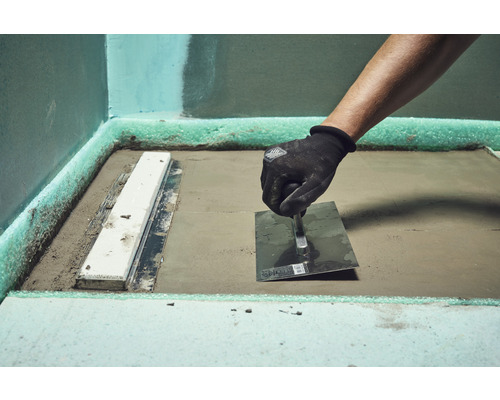 Vakman bewerkt dekvloer met een troffel in een badkamer