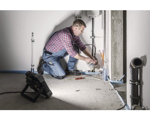 Installateur werkt aan leidingen in een lichte ruimte. Gereedschap en een lamp zijn op de voorgrond.