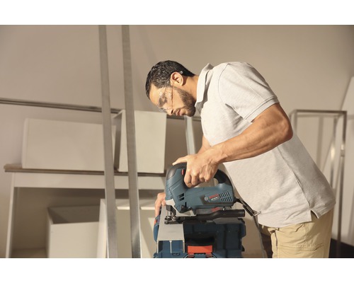 Een man met een veiligheidsbril zaagt een werkstuk met een decoupeerzaag.