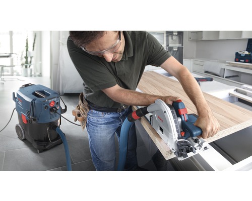 Ambachtsman werkt met een invalzaag aan een houten plaat, aangesloten op een industriële stofzuiger van Bosch.