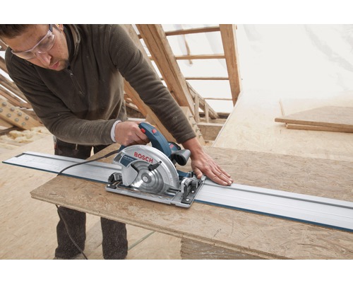 Ambachtsman zaagt een houten plank met een cirkelzaag, ondersteund door een geleiderail. Bosch logo zichtbaar.