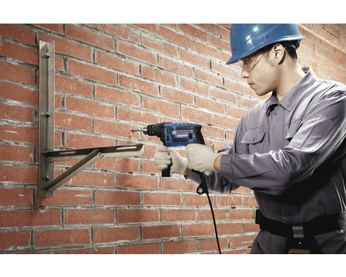 Vakman boort met een klopboormachine in een bakstenen muur