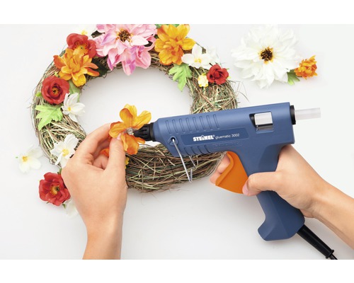 Decoratieve krans wordt versierd met een lijmpistool en kunstbloemen.