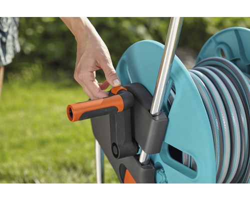 Een persoon bedient een haspel om een tuinslang op te rollen.