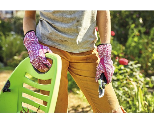 Vrouw met tuinhandschoenen, snoeischaar en kruiwagen in de tuin.