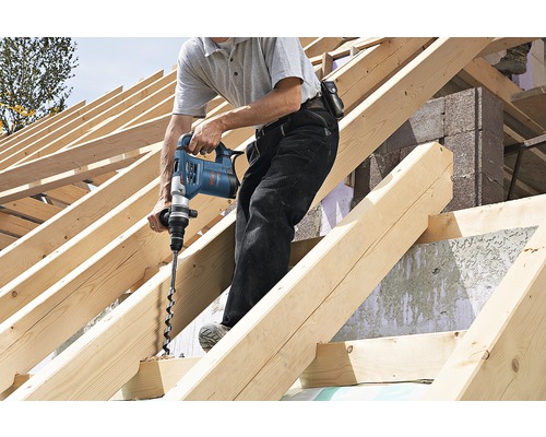 Man boort met een boormachine een gat in een houten balk op een bouwplaats