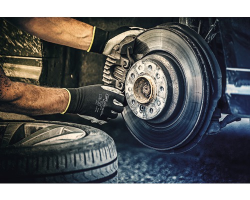 Monteur met veiligheidshandschoenen die de remmen van een voertuig repareert.