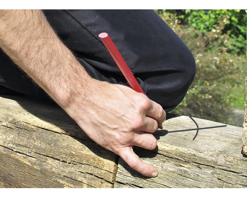 Een persoon tekent een markering op een stuk hout met een timmermanspotlood.