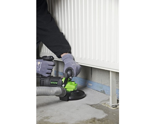 Een persoon gebruikt een betonschuurmachine in de buurt van een radiator.