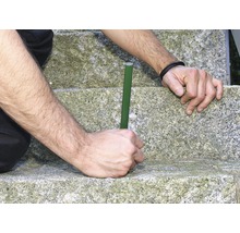 Persoon plaatst een groene plantenstaaf in een stenen trap.