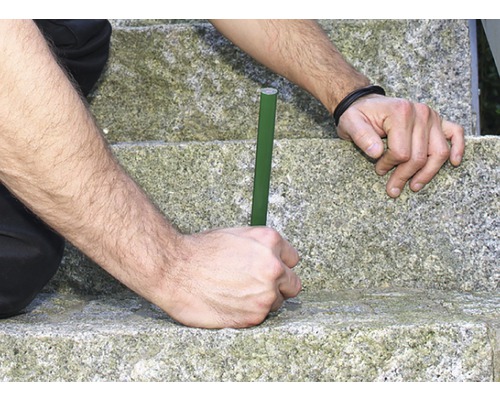 Persoon plaatst een groene plantenstaaf in een stenen trap.