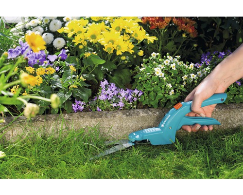 Persoon die gras snijdt met een Gardena grasschaar voor een bloembed.