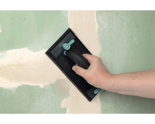 Hand schuurt vulmiddel op een muur met een handschuurmachine