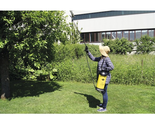 Vrouw besproeit boom met rugspuit in tuin