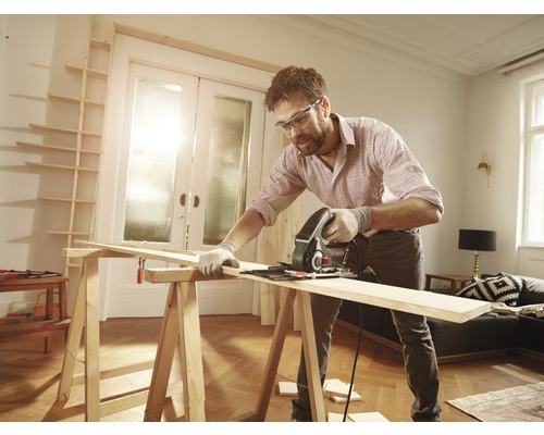 Een man zaagt een houten plank met een cirkelzaag in een kamer op een zaagbok.