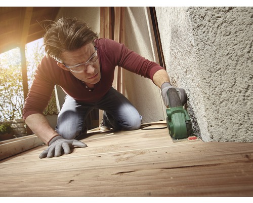 Een man schuurt hout met een multislijper. Hij draagt een veiligheidsbril en handschoenen.
