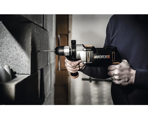 Een persoon boort met een accuboormachine in een stenen muur. Het Worx logo is zichtbaar.