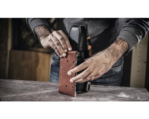 Een persoon verwisselt schuurpapier op een bandschuurmachine.