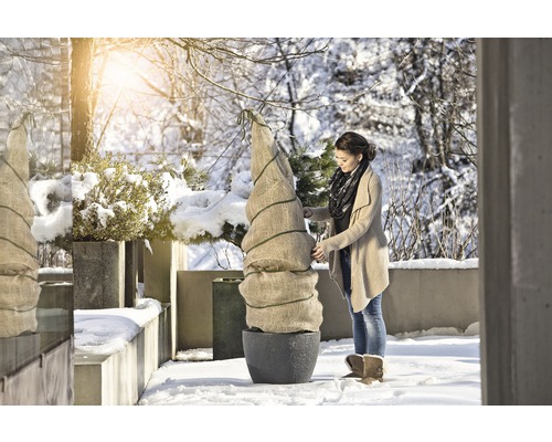 Vrouw verpakt plant in pot met winterbescherming in de tuin