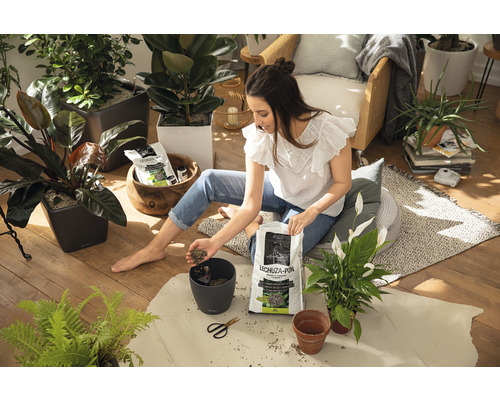 Vrouw zit op de vloer en vult een plantenpot met Lechuza Pon plantensubstraat, omringd door kamerplanten