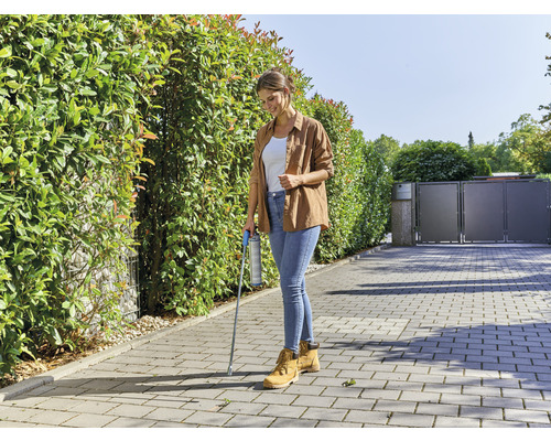 Vrouw gebruikt onkruidverdelger met spuitlans op straatstenen voor een haag.