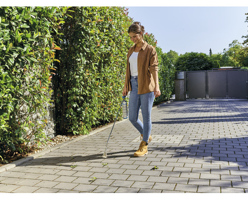 Vrouw verwijdert onkruid met een onkruidsteker op een verhard pad