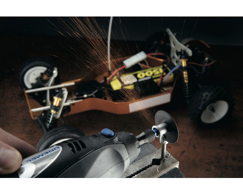 Dremel Logo. Een persoon bewerkt een werkstuk met een Dremel multitool, er vliegen vonken af. Op de achtergrond is een modelauto te zien.