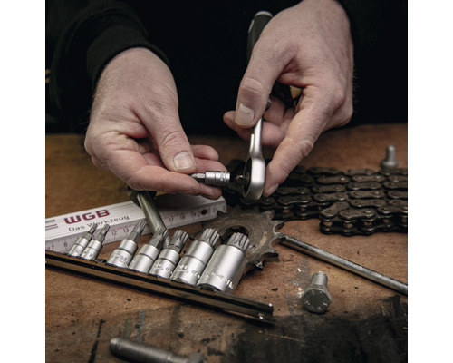 Een man gebruikt een ratelsleutel met een bitset op een werkbank met gereedschap en kettingen.