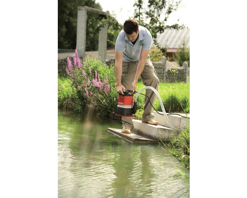 Man bedient een vuilwaterpomp aan de oever van een water.