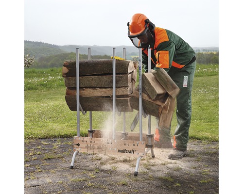 Een persoon met beschermende kleding zaagt hout met een kettingzaag op een houtzaagbok van Wolfcraft