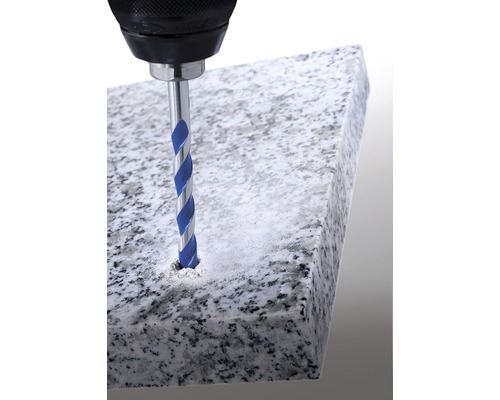 Een boormachine boort met een steenboor een gat in een stenen plaat.