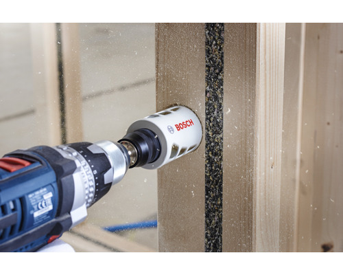 Boormachine met Bosch gatenzaag boort een gat in een houten plank.