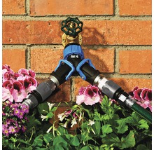 Waterkraan met verdeler en aangesloten tuinslangen voor een bakstenen muur