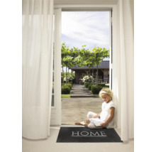 Een jong meisje zit te lezen op een deurmat met het woord ''Home'' voor een open terrasdeur met uitzicht op een tuin