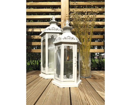 Twee witte lantaarns van metaal en glas op een houten terras, daarnaast een glazen vaas met droogbloemen