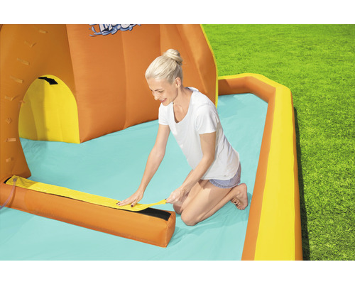 Opblaasbare waterglijbaan met plonsbad en vrouw bij de installatie in de tuin.