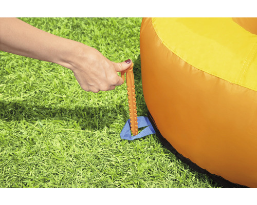 Bevestiging van een oranje luchtzitzak met een haring in het gras