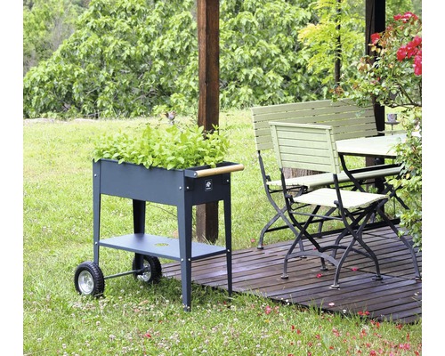 Tuinscene met een metalen kruidenwagen, een tuintafel en een tuinbank op een houten terras.