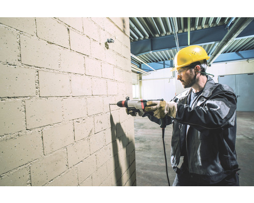 Een man boort met een klopboormachine een gat in een bakstenen muur.
