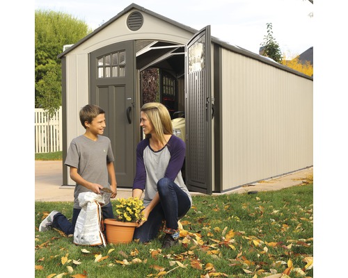 Tuinscène met moeder en zoon voor een tuinhuisje die bloemen verpotten.