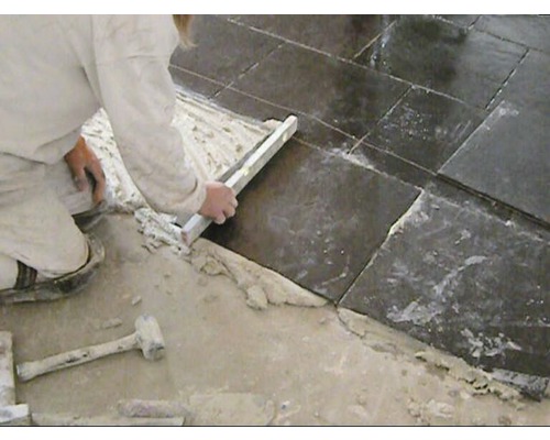 Een persoon legt vloertegels met een waterpas en een hamer.