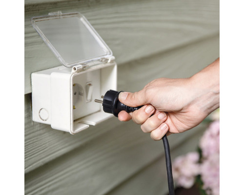 Een persoon steekt een stekker in een waterdicht stopcontact voor buiten.